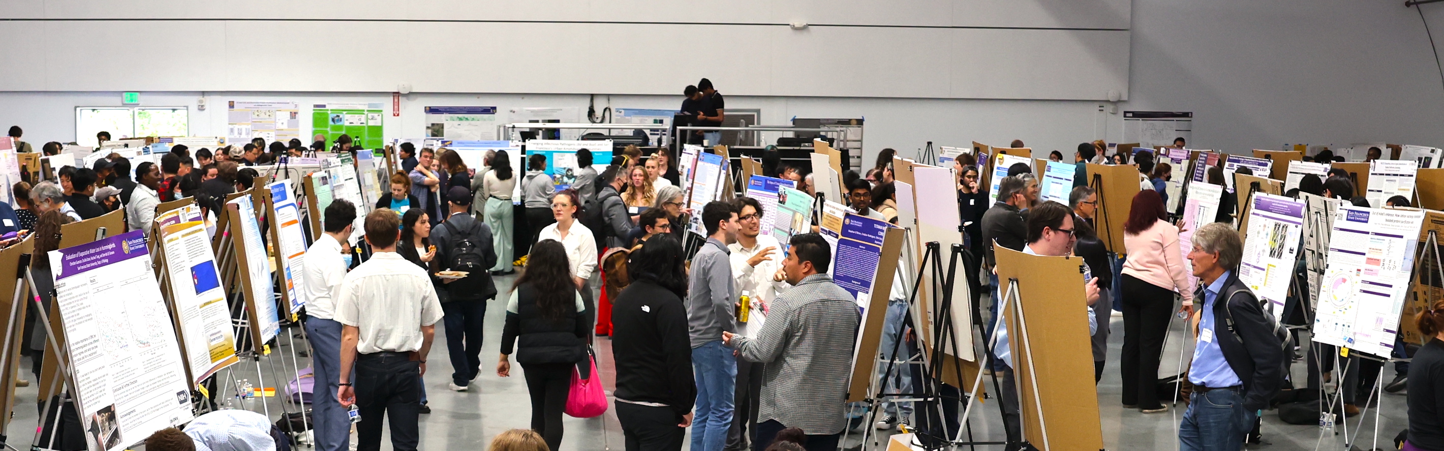 People walking around a showcase event, looking at posters on easels.