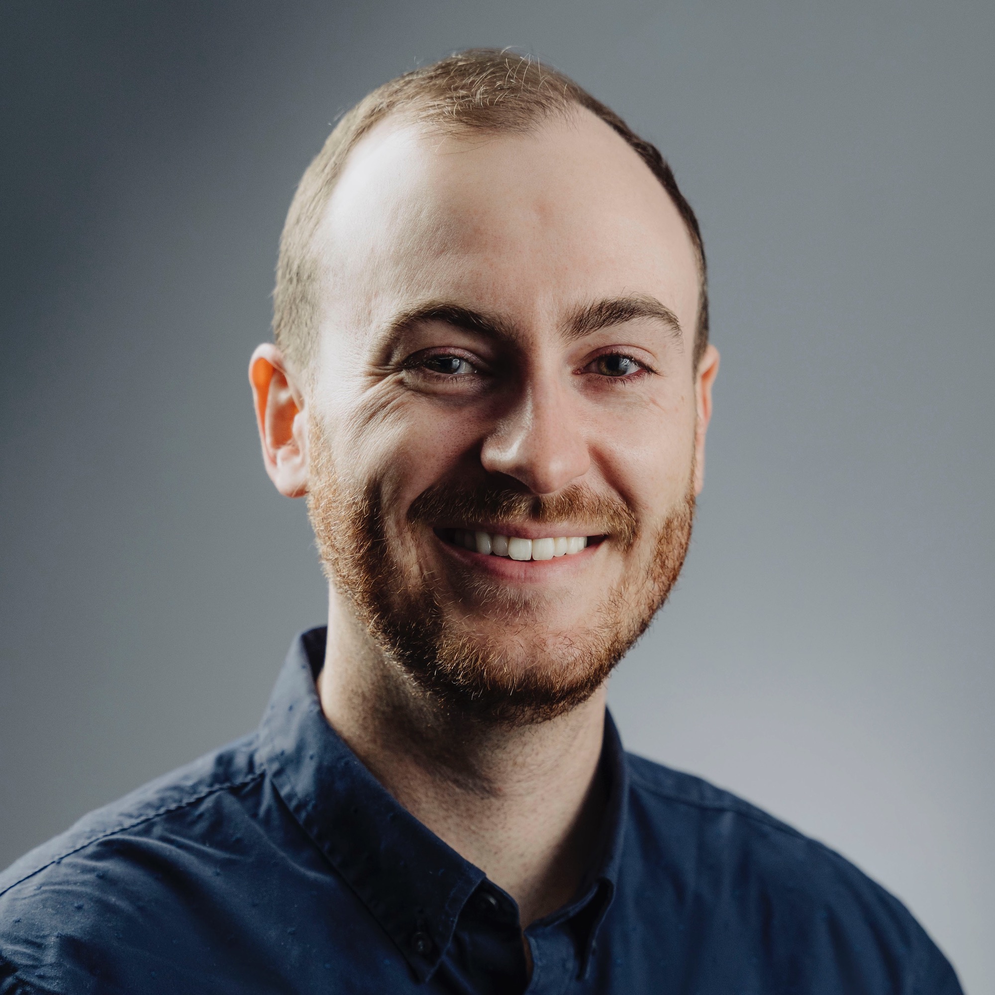 William Brogan, headshot of man with beard and mustache, smiling, wearing a blue button-down shirt